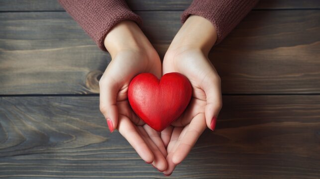 Close-up of a woman's hands holding a red heart on a wooden background. Valentine's Day greeting card. A symbol of love. View from above.