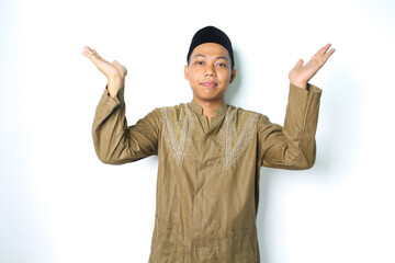 pleased asian muslim man wearing koko clothes presenting with open palm to above isolated on white...