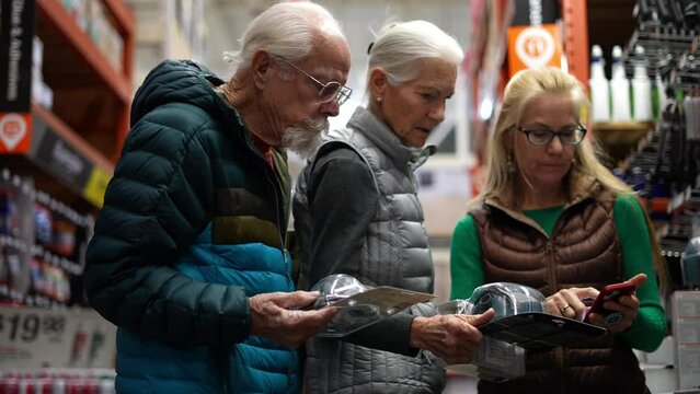 Elderly man and woman, with younger mature woman compare products in a big box hardware store.
