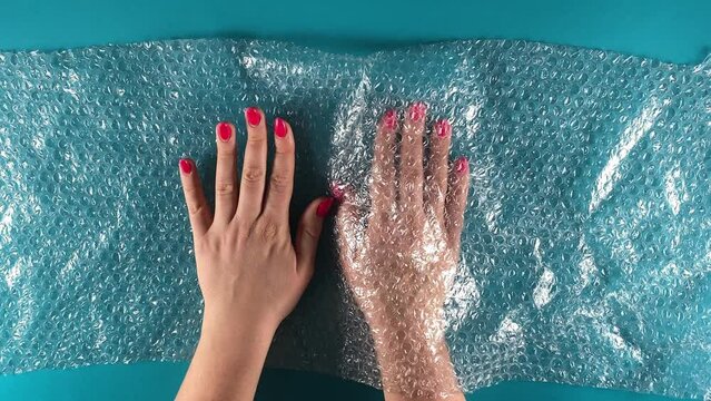 An allegory conveying abstract meaning on plastic pollution. Natural vs artificial concept. Unrecognizable female compares hands by using bubble wrap. Indoors studio shot isolated on blue background