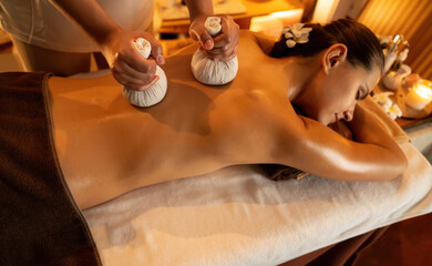 Hot herbal ball spa massage body treatment, masseur gently compresses herb bag on woman body....
