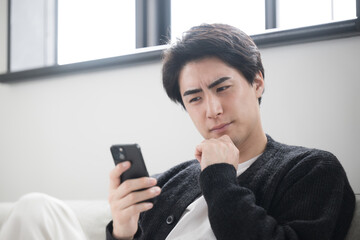 綺麗な白いリビングでスマホを見るくつろぐ長袖の男性...