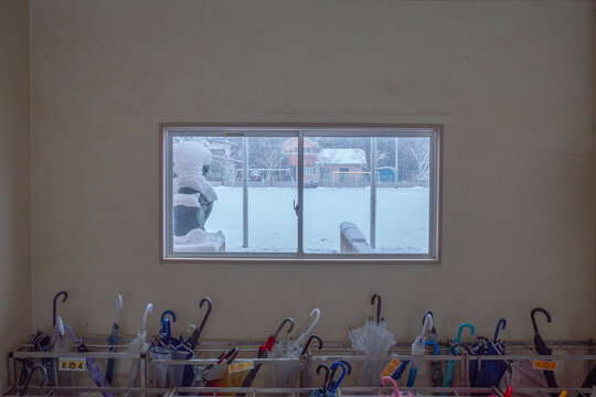 雪が降る日の小学校の昇降口・傘立てと窓から見える校庭/スクールライフ