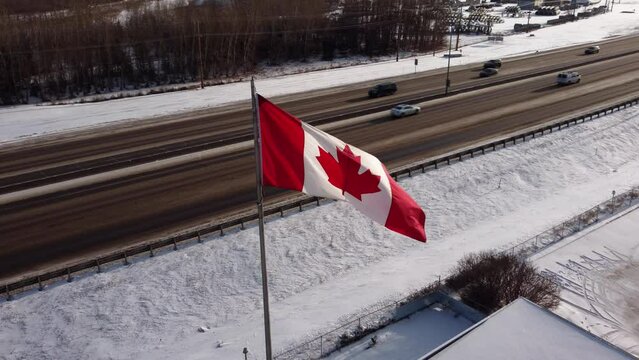 Waving Canadian flag with a highway in the background on a sunny winter day.