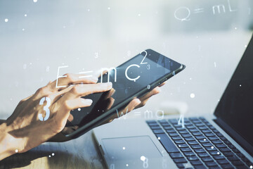 Creative scientific formula hologram and hand working with a digital tablet on background, research concept. Multiexposure