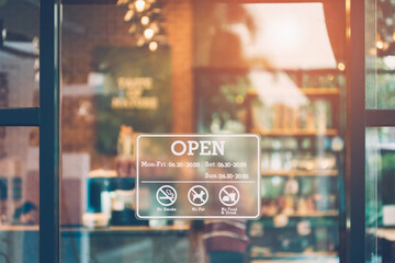 Stickers showing opening and closing times. Close up an open sign on the front window of a coffee shop/cafe and a blurred, bokeh image inside the shop.