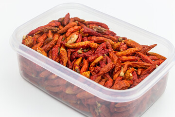 Dried red hot chili peppers in plastic box on white background.