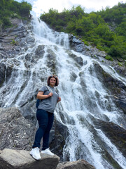 Woman with backpack standing near beautiful waterfall