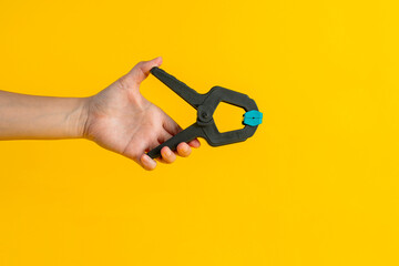 Black plastic spring clamp in hand isolated on yellow background