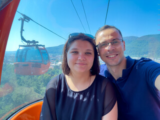 A guy and a girl ride in an orange telegondola, cable car