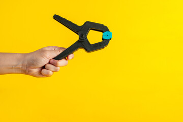Black plastic spring clamp in hand isolated on yellow background