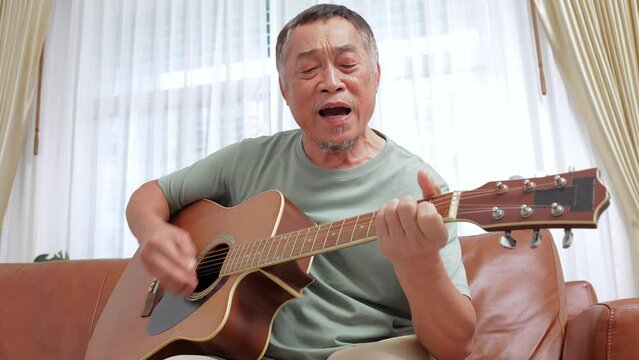 Elderly Asian man playing guitar and singing at home He is happy with his retired life. music concept, live performance
