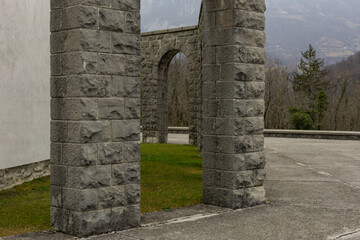 Old mausoleum or kostnica at kobarid, as seen from the terraces. Visible stone pillars and the church on the middle, on a cloudy day.