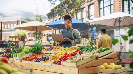 Successful Female Farmer Working on a Laptop Computer, Catching Up with Supplier Online to Plan Future Orders for Her Organic Street Vendor Stall with Sustainable Fruits and Vegetables
