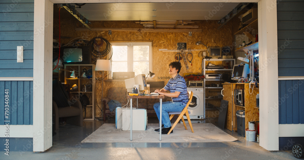 Poster caucasian male software engineer entering retro garage and sitting at his work desk with old desktop