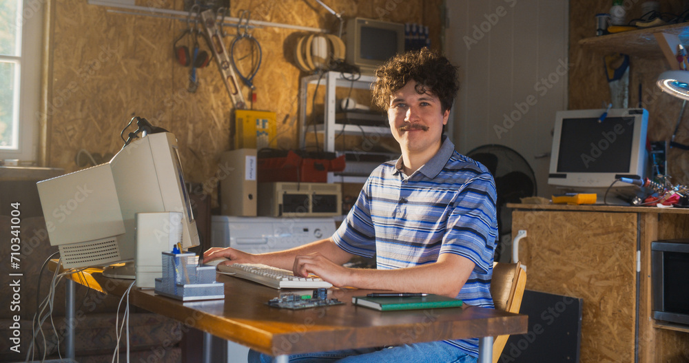Poster Caucasian Male Software Engineer Programming On Old Desktop Computer In Retro Garage, Looking At Camera And Smiling. Man Starting an Innovative Startup Company In Nineties. Nostalgia Concept.