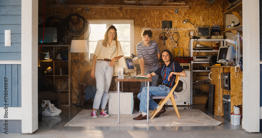 Poster diverse team of three young startup company founders in retro garage with old desktop computer. male