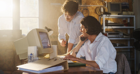 Two Caucasian Male Stock Brokers Working In Retro Garage, Using Old Desktop Computer With...