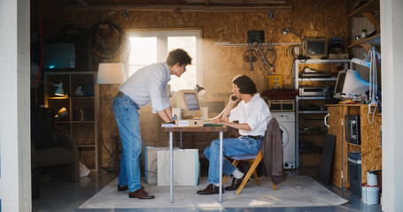 Two Caucasian Male Stock Traders Working In Retro Garage, Using Old Computer With Candlestick Chart And Landline Phone To Pitch A Public Company To Investors. Partners Celebrating Successful Sale.
