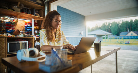 Happy Hispanic Woman Using Laptop Computer In Opened Garage. Successful Female Digital Entrepreneur...