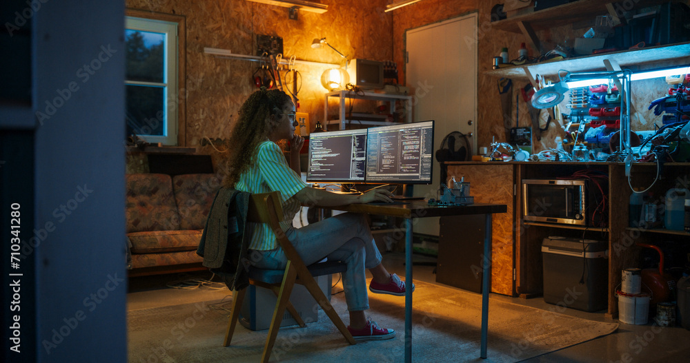 Poster Hispanic Female Programmer Writing Code On Desktop Computer In Garage At Home. Woman Working On Innovative Software As A Service Startup For Business At Night. Digital Entrepreneur Starting Company.