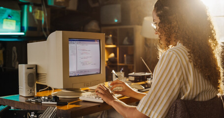 Side View Of Hispanic Female Engineering Student Writing Academic Thesis On Old Desktop Computer In Retro Garage. Future Engineer Focused On Innovative Project For University Of Technology In Nineties