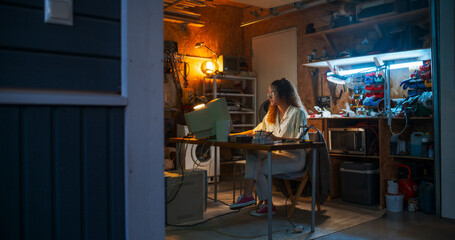Fototapeta na wymiar Wide Shot Of Hispanic Female Engineer Using Old Computer In Nineties Retro Garage In The Evening. Intelligent Woman Programming, Working On Innovative Portable Device, Starting Technological Company.