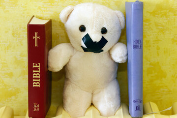 Bibles and teddy bear with tape on his mouth. Symbol of silence on child abuse and victim in...