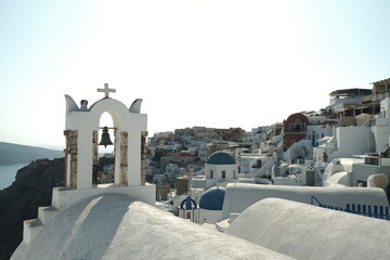 Church bell in front of Santorini white houses - obrazy, fototapety, plakaty