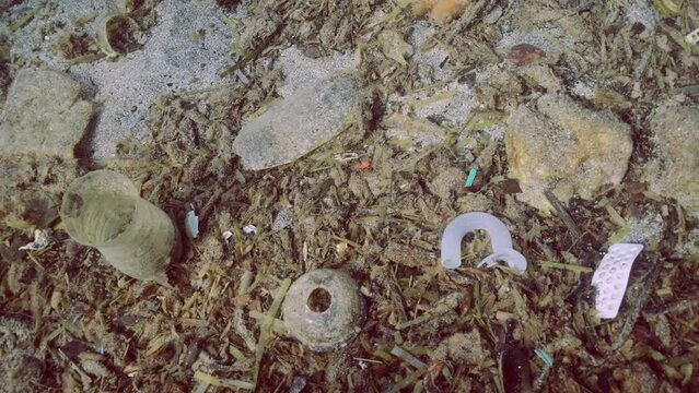 Close up of rock-sand seabed covered with plastic trash and oter debris. Concept plastic pollution of Ocean 