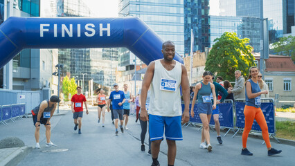 Diverse Group of People Crossing the Finish Line in a City Marathon During the Day. Tired Runners...