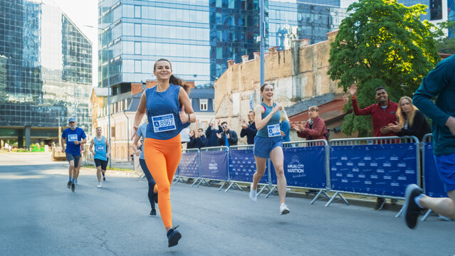 Diverse Group of People Running a Marathon in a City During the Day. Active and Fit Smiling Female Runner Competing to Reach the Finish Line, Supported by Friends and Family