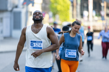 Portrait of Smiling Young Black Man Running in a City Marathon, Waving at the Supportive Audience....