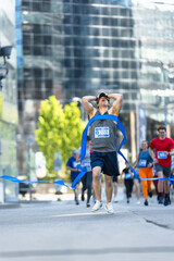 Portrait of Athletic Male Jogger Crossing the Finish Line in Marathon with the Audience Cheering. Happy Successful Man Celebrating Winning, Achieving his Goal at Finishing First in a Race