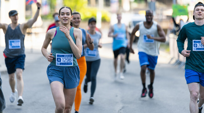 Diverse Group of People Running a Marathon in a City During the Day. Active and Fit Smiling Female Runner Competing to Reach the Finish Line, Supported by Friends and Family
