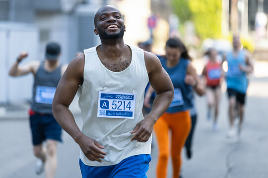 Portrait of Smiling Young Black Man Running in a City Marathon, Waving at the Supportive Audience. Friendly Happy Male Runner Celebrating Crossing the Finish Line in a Race