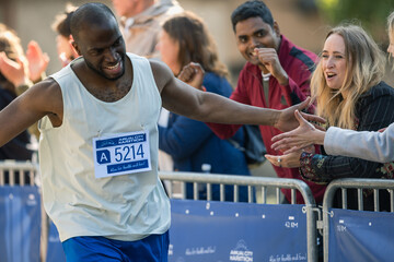 Marathon Audience Clapping and Cheering Their Loved Ones Participating in the Race: Black Athletic Male Marathon Runner Giving a High Five to Female Friend Supporting Him in the Audience While Running - obrazy, fototapety, plakaty