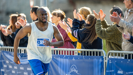 Portrait of Smiling Young Black Man Running in a City Marathon, Waving at the Supportive Audience....