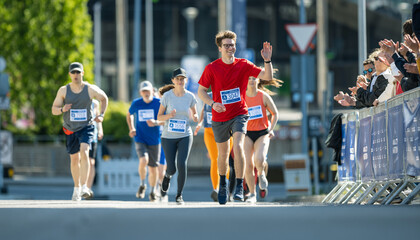 Shot of a Group of Diverse People Running in a Marathon and Waving to their Loved Ones and...