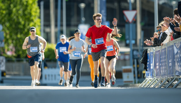 Shot of a Group of Diverse People Running in a Marathon and Waving to their Loved Ones and Supporters in the Audience. Runners Participating in a Charity Run to Raise Money a Cause