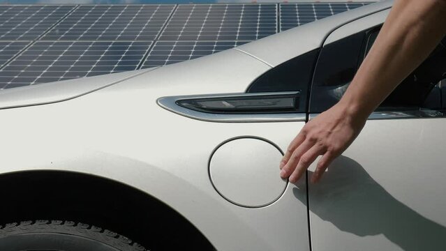 Male hand connects power cable supply to charge EV or electric car on the solar panels background. Unrecognizable man plugging in an electric auto or PHEV at photovoltaic charging station
