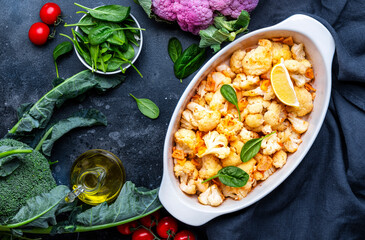 Baked cauliflower in garlic and lemon dressing with olive oil in ceramic baking dish, gray background, top view