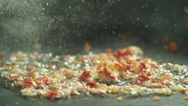 Garlic and red chili frying with olive oil in steel pan hot and boiling slow motion