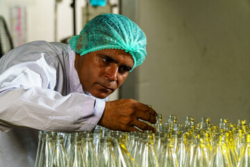 A factory worker inspects bottles on a beverage production line.