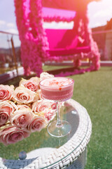 Pink alcoholic cocktail on a table with roses on the background of a pink terrace. Barbie concept