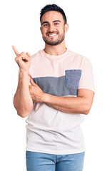 Young handsome man wearing casual clothes with a big smile on face, pointing with hand and finger to the side looking at the camera.