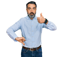 Middle aged man with beard wearing business shirt doing thumbs up and down, disagreement and agreement expression. crazy conflict