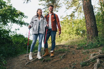 A happy couple is hiking in the mountains. A boy is holding his sunglasses while a girl is using trekking poles.