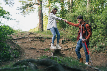A boy is helping a girl to climb down safely during their hike in the woods.