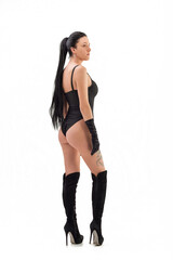 Fototapeta premium A gorgeous slim, tanned brunette with a perfect body in a black bodysuit and boots poses against a white background in the studio. Hair removal.